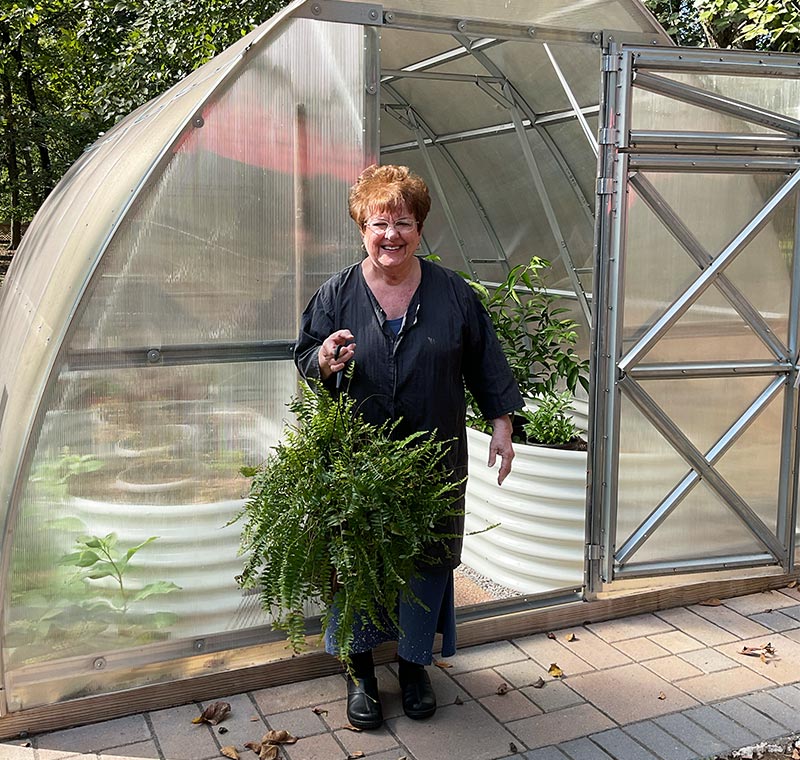 cindas-botanical-blends-cinda-holding-plant-in-front-of-greenhouse